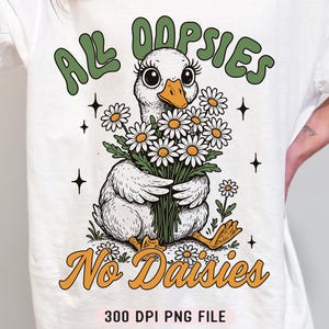 May include: White t-shirt with a green and white illustration of a duck holding a bouquet of daisies. The text "All Oopsies No Daisies" is printed on the shirt.