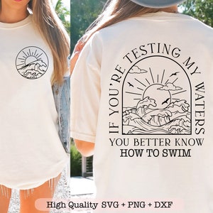 May include: A white t-shirt with a black graphic of a sun, clouds, and waves. The text "If you're testing my waters you better know how to swim" is printed on the back of the shirt.