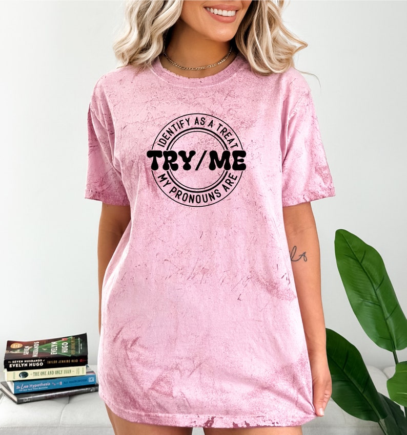 Puede incluir: Una camiseta rosa tie-dye con un gr&aacute;fico circular negro que dice "Identify as a treat, Try/Me, My pronouns are".