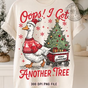 May include: Cream-colored t-shirt featuring a goose wearing a Santa hat and a red sweater, pulling a cart with a Christmas tree and gifts. Text reads "Oops! I Got Another Tree" and "Merry Goosemas."