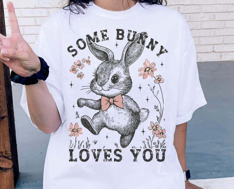 Peut inclure: T-shirt blanc avec une illustration en noir et blanc d'un lapin avec le texte "Some Bunny Loves You" en noir.
