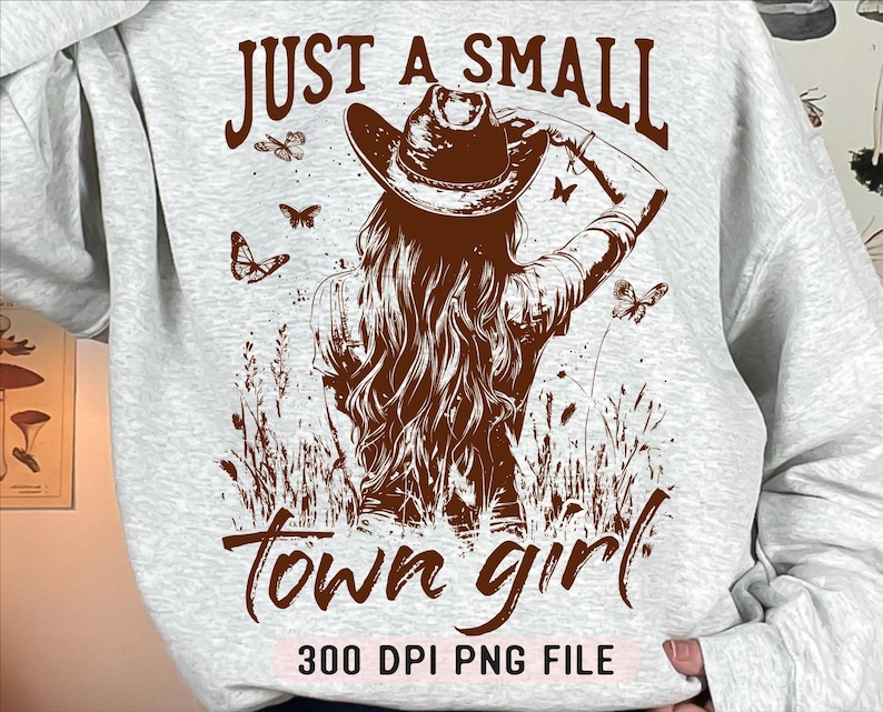 May include: A gray sweatshirt with a brown graphic design of a woman wearing a cowboy hat and the text "Just a small town girl 300 DPI PNG FILE".
