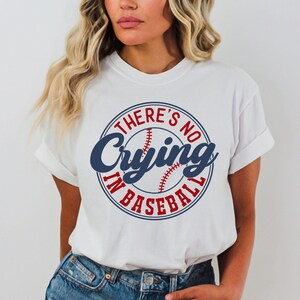 May include: White t-shirt with a blue and red baseball graphic and the text "There's No Crying In Baseball".