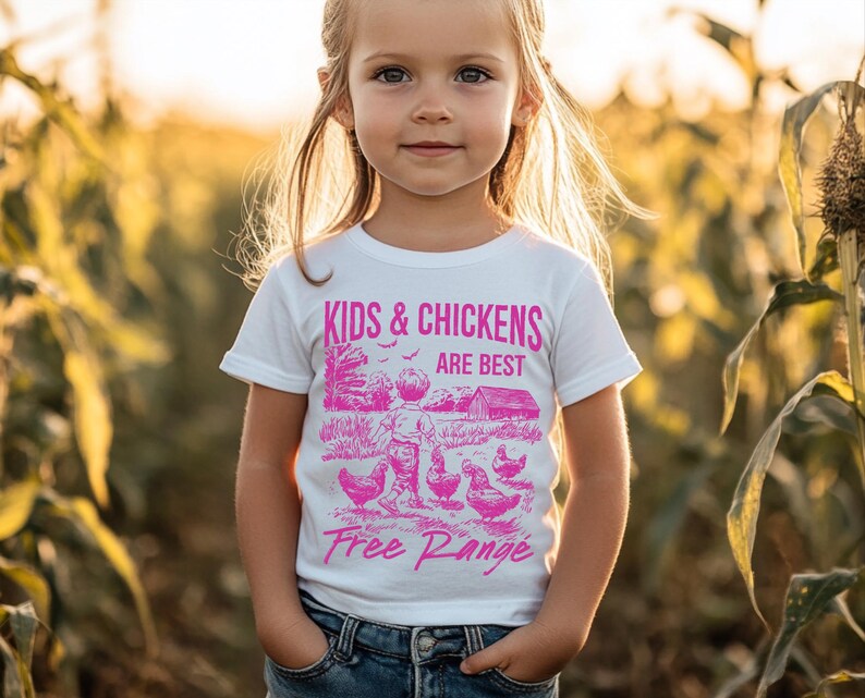 K&ouml;nnte beinhalten: Ein wei&szlig;es T-Shirt mit einem pinkfarbenen Grafikdesign, das ein Kind und H&uuml;hner zeigt. Die Grafik lautet "Kids & Chickens Are Best Free Range".