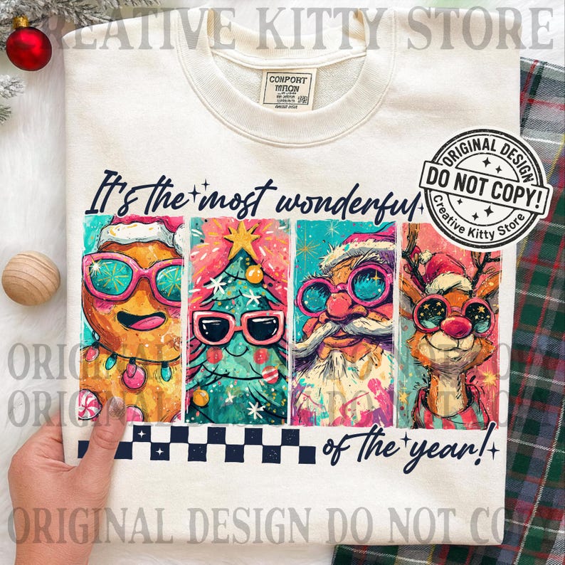 May include: Cream-colored sweatshirt with a colorful Christmas-themed graphic. The graphic features a gingerbread man, Christmas tree, Santa Claus, and reindeer, all wearing sunglasses. Text reads "It's the most wonderful of the year!"