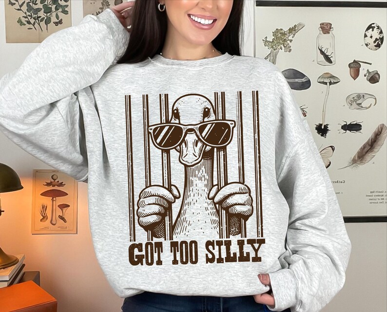 Pu&ograve; includere: Una felpa grigia con una grafica di un'anatra con occhiali da sole e il testo "Got Too Silly".