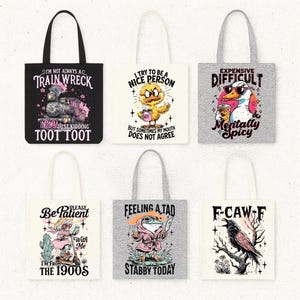 May include: Collection of tote bags with humorous designs. One bag is black with a train graphic and the text "I'm not always a train wreck." Other bags feature a duck, frog, and raven with witty phrases like "Mentally Spicy" and "Stabby Today."