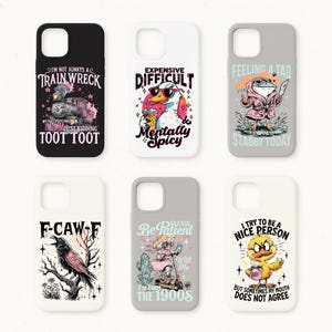 May include: A collection of six phone cases with humorous designs. The cases feature illustrations of a train, a duck with sunglasses, a frog in a robe, a raven, a woman on a scooter, and a chick. Each case has a unique phrase.