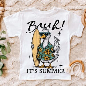 May include: White t-shirt with a cartoon duck wearing sunglasses and a floral shirt holding a surfboard. The text "Bruh! It's Summer" is printed on the shirt.