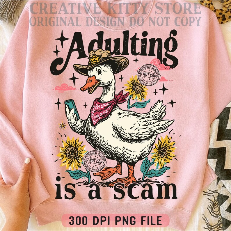 May include: Pale pink sweatshirt featuring a cartoon goose in a cowboy hat and bandana, holding a phone. The text "Adulting is a scam" is below the goose, with sunflowers and stars. The words "Original Design Do Not Copy" are also visible.