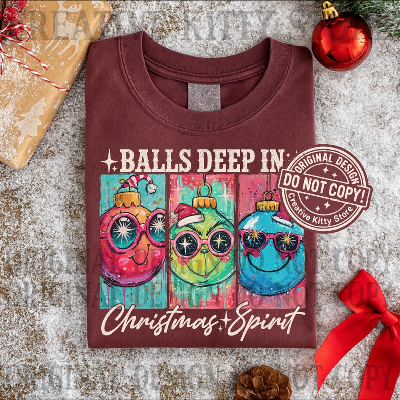 May include: Burgundy t-shirt with a graphic of three Christmas ornaments wearing sunglasses and Santa hats. The text reads "BALLS DEEP IN Christmas + Spirit". A "Do Not Copy" sticker is visible.