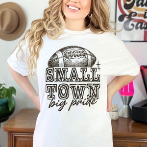May include: White t-shirt with a black and white illustration of a football and the text "Small Town Big Pride".