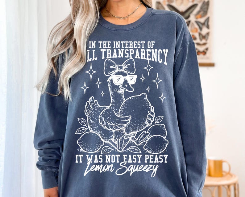 May include: A dark blue sweatshirt with a white graphic of a duck wearing sunglasses and holding lemons. The text on the sweatshirt reads "In the interest of full transparency it was not easy peasy lemon squeezy."