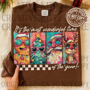 May include: Brown sweatshirt with a colorful graphic featuring a gingerbread man, Christmas tree, Santa Claus, and reindeer, all wearing sunglasses. The text reads "It's the most wonderful time of the year!"