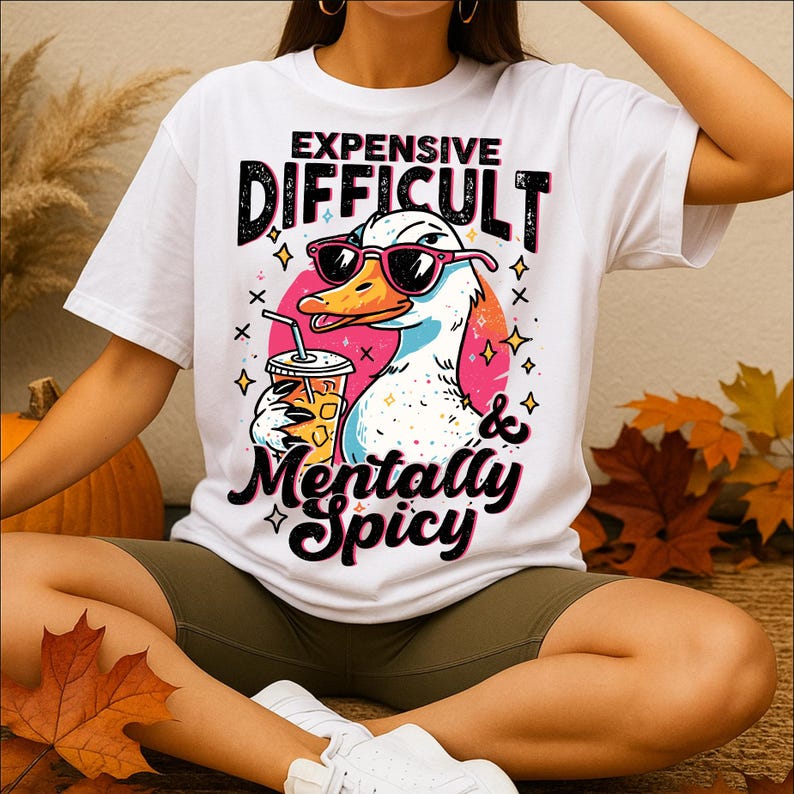 Pu&ograve; includere: T-shirt bianco con grafica di un'anatra con occhiali da sole e una bevanda. Il testo sulla maglietta recita "EXPENSIVE DIFFICULT & Mentally Spicy". L'anatra &egrave; ambientata su un cerchio rosa con stelle e croci.