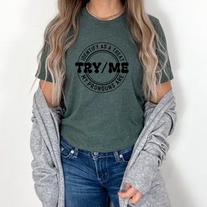 Puede incluir: Una camiseta verde oscuro con un gr&aacute;fico circular negro que dice "Identify as a treat, my pronouns are try/me".