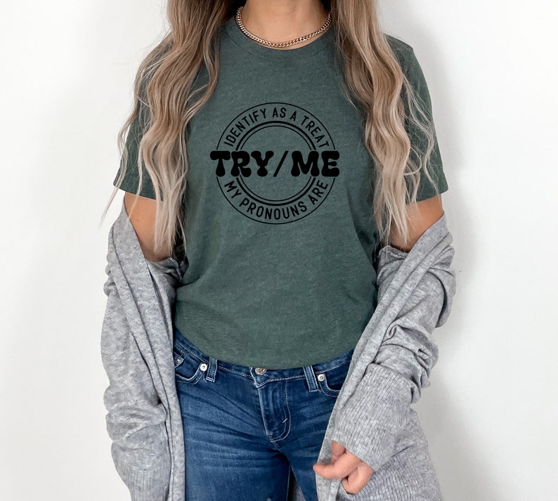 Puede incluir: Una camiseta verde oscuro con un gr&aacute;fico circular negro que dice "Identify as a treat, my pronouns are try/me".