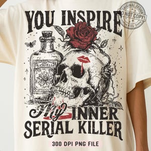 May include: Cream-colored t-shirt featuring a graphic design with a skull, red rose, and a bottle labeled "BASSISSAR." The text reads "YOU INSPIRE My INNER SERIAL KILLER." A red lip with a blood drop is on the skull. The design includes a butterfly and other details.