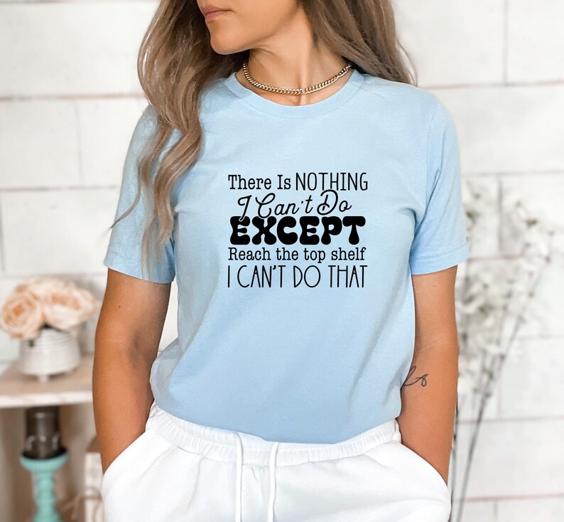 May include: A light blue t-shirt with a black graphic that reads "There is NOTHING I Can't Do EXCEPT Reach the top shelf I CAN'T DO THAT".