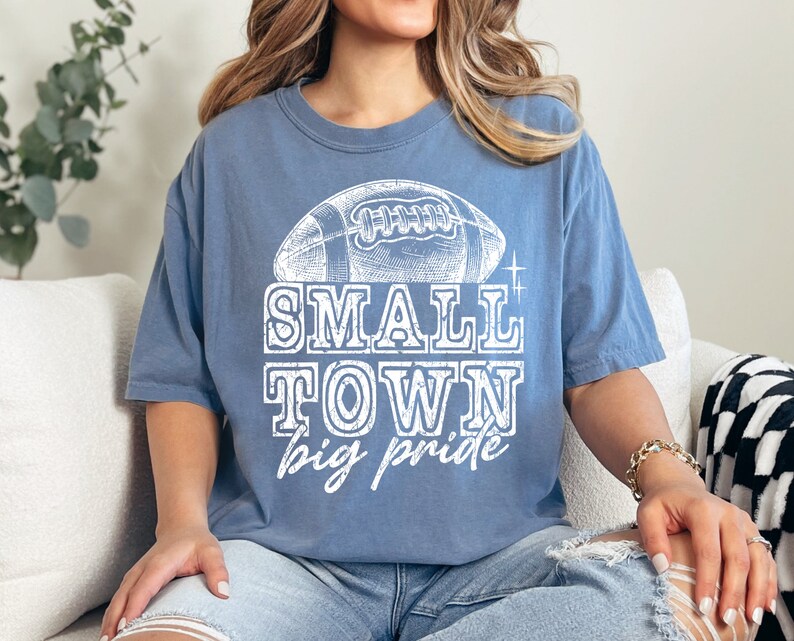 May include: A blue t-shirt with a white vintage-style graphic of a football and the text "SMALL TOWN big pride".