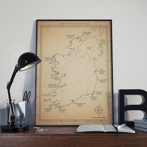 May include: Framed nautical chart of Ireland with lighthouse locations, in a vintage style. The map is tan with black text and a compass rose. A black desk lamp, office supplies, and books are on the desk.