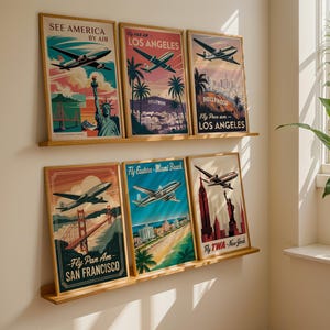 以下が含まれることがあります： 飛行機のイラストが描かれた、額入りのヴィンテージ旅行ポスターのコレクション。ニューヨーク、サンフランシスコ、マイアミビーチなど、アメリカの象徴的な場所が描かれています。青、赤、オレンジの色合いで、レトロな雰囲気を醸し出しています。