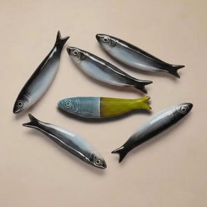 Pu&ograve; includere: Sei statuette di pesci in ceramica in vari colori. I pesci hanno un design elegante con colori nero, bianco e blu. Un pesce &egrave; diviso con blu e giallo. Le statuette sono disposte su uno sfondo neutro.