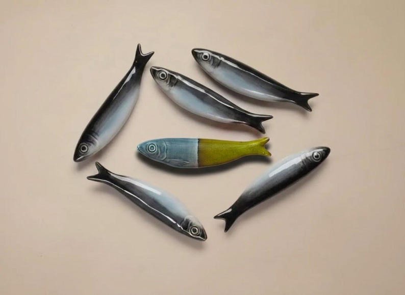 Pu&ograve; includere: Sei statuette di pesci in ceramica in vari colori. I pesci hanno un design elegante con colori nero, bianco e blu. Un pesce &egrave; diviso con blu e giallo. Le statuette sono disposte su uno sfondo neutro.