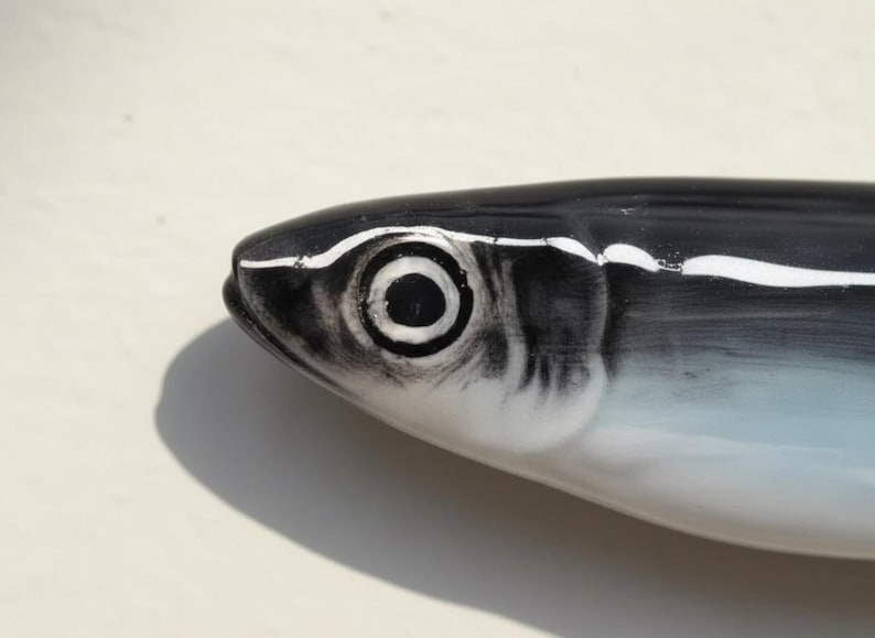 May include: A ceramic fish figurine with a black and white design. The fish has a detailed eye and a streamlined body. The color palette includes black, white, and shades of blue, creating a realistic appearance. The figurine is likely a decorative item.