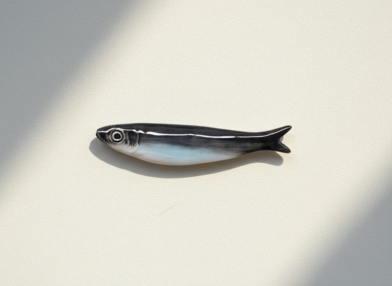 May include: A ceramic fish figurine with a black and white design. The fish has a white underbelly and a dark gray back. The figurine is approximately 6 inches long and has a detailed eye.