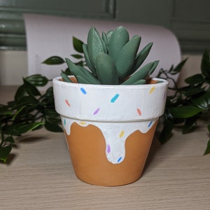 May include: A small succulent plant in a terracotta pot with white paint and colourful sprinkles. The pot has a white glaze that drips down the sides.