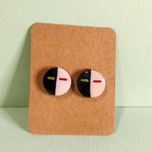 May include: A pair of round earrings in black and white with green and red accents. The earrings are displayed on a brown card.