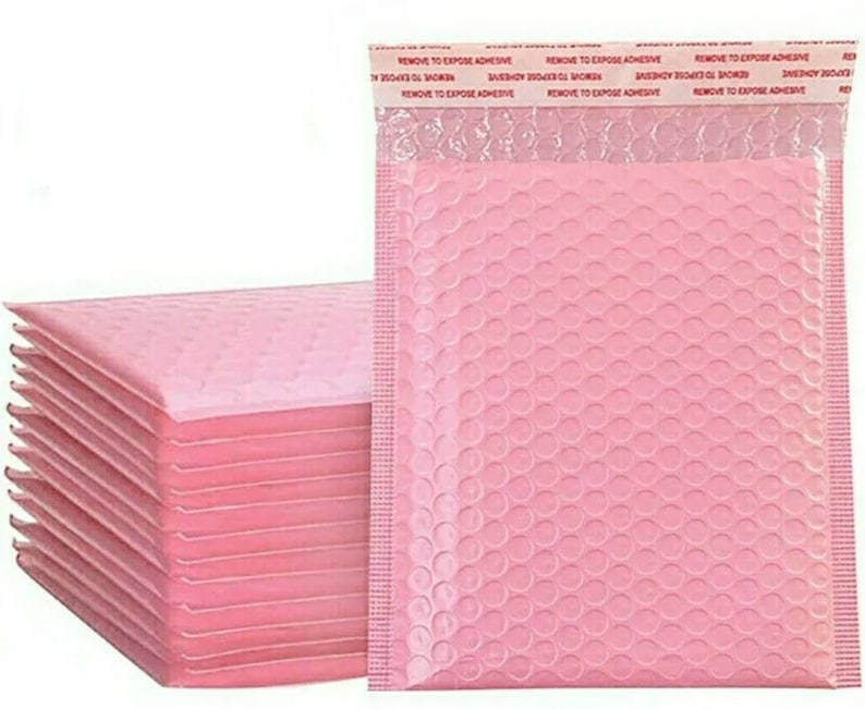 May include: A stack of ten pink bubble mailers with a single mailer standing upright. The mailers have a white adhesive strip with the text "REMOVE TO EXPOSE ADHESIVE" printed in red.