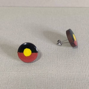 Op de afbeelding: Een paar oorbellen met de Aboriginal vlag. De oorbellen zijn gemaakt van hout en hebben een ronde vorm. De vlag is geschilderd in de traditionele kleuren zwart, rood, geel en wit.