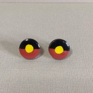 Op de afbeelding: Een paar kleine, ronde oorbellen met de Aboriginal Australische vlag. De oorbellen zijn rood, zwart en geel met een cirkel in het midden.