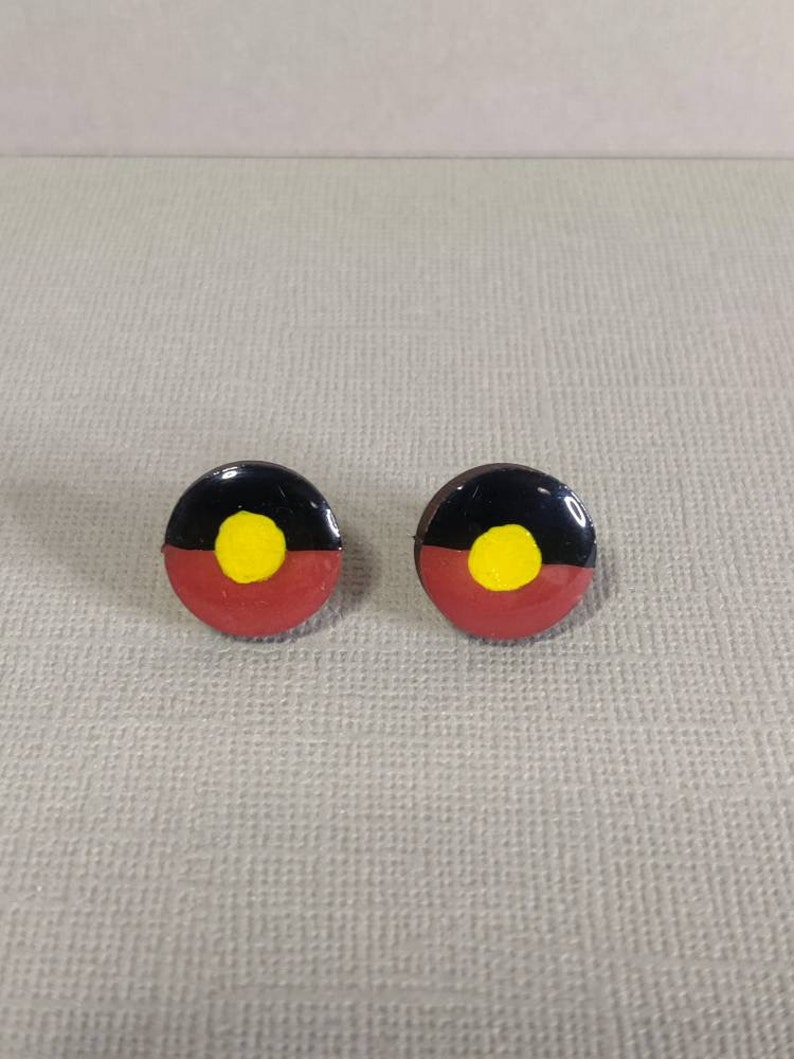 Op de afbeelding: Een paar kleine, ronde oorbellen met de Aboriginal Australische vlag. De oorbellen zijn rood, zwart en geel met een cirkel in het midden.