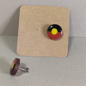 Op de afbeelding: Een paar oorbellen met de Aboriginal Australian vlag. De oorbellen zijn gemaakt van hout en hebben een zilveren post.