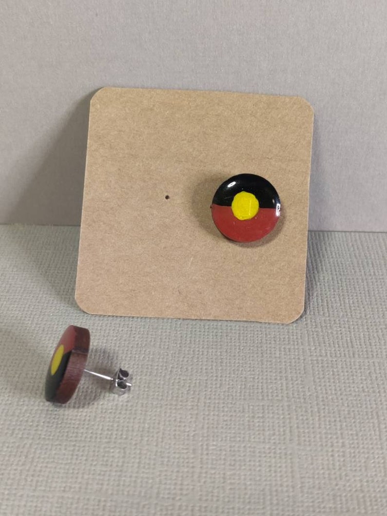 Op de afbeelding: Een paar oorbellen met de Aboriginal Australian vlag. De oorbellen zijn gemaakt van hout en hebben een zilveren post.