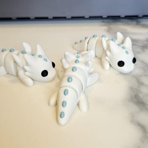 May include: Three white ceramic dragon figurines with blue accents. The dragons are segmented and have a whimsical, cartoon-like appearance.