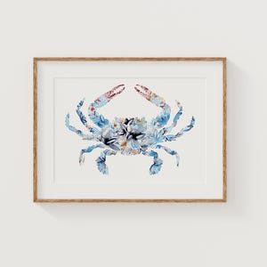 May include: A framed watercolor print of a crab. The crab is composed of blue, white, and floral patterns. The claws are red and pink. The artwork is set against a white background and framed in a light brown wooden frame.