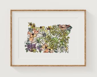 May include: A framed art print featuring a floral arrangement in the shape of the state of Oregon. The artwork showcases a variety of flowers in shades of yellow, orange, pink, and purple, outlined with black ink. The frame is a light brown color.