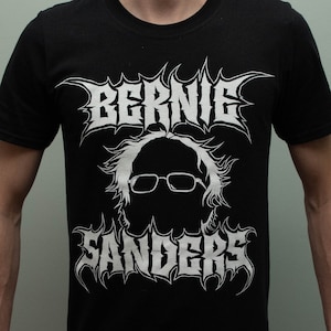 Könnte beinhalten: Schwarzes T-Shirt mit einem weißen Aufdruck von Bernie Sanders' Gesicht in einer Metal-Band-Schriftart. Der Text lautet "Bernie Sanders".