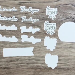 May include: A collection of die-cut stickers featuring the phrases Best wishes, Thank you, and Have a LOVELY day in various script fonts. The set includes several white blank labels in rectangular, circular, and irregular shapes for custom writing.