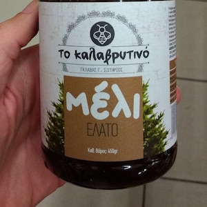 May include: A glass jar of honey with a white label that says "To kalafrytivó" in Greek. The label also says "Gkalavas G. Sotirios" and "Méli Elato" in Greek. The jar is 450 grams.