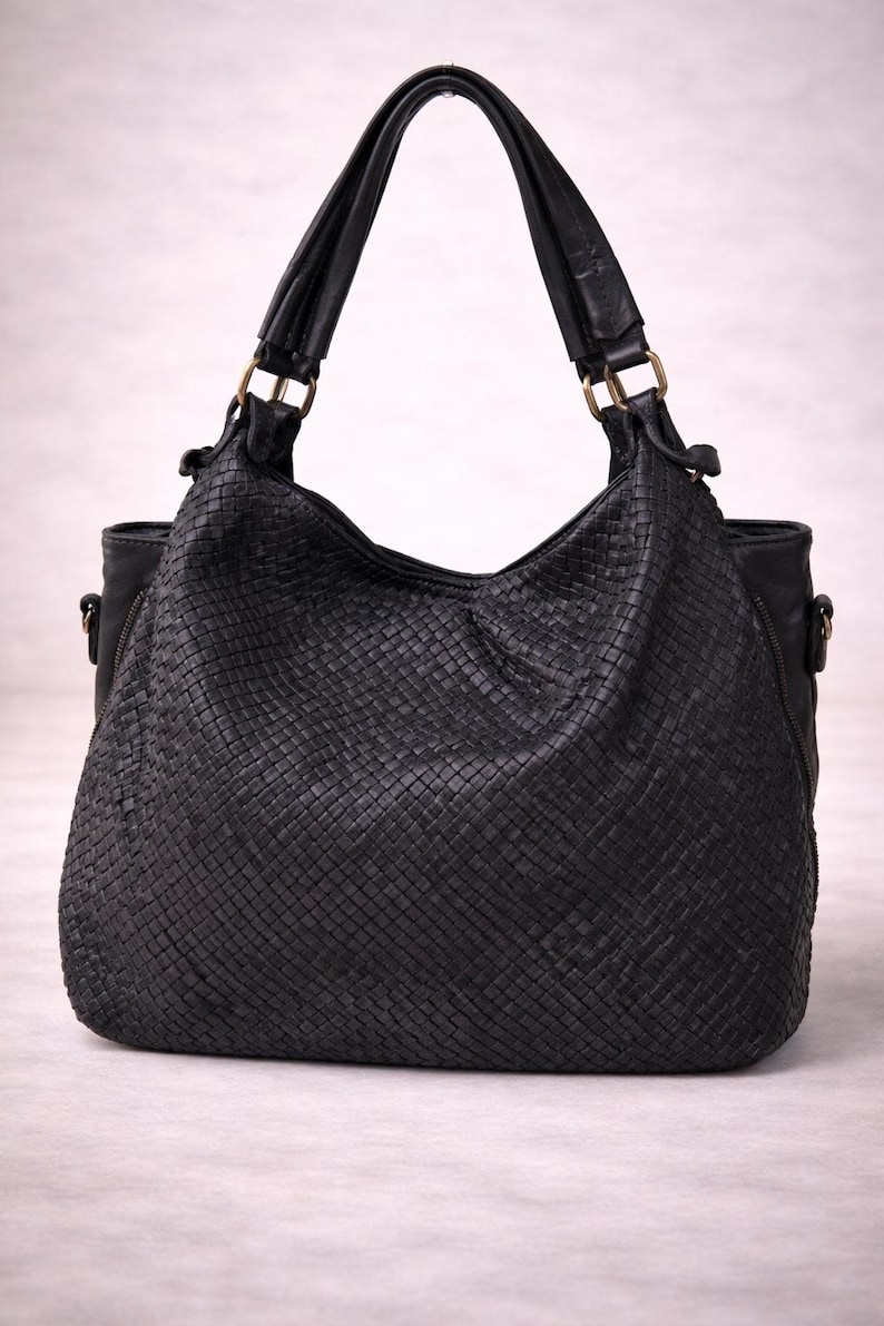 May include: Black woven leather shoulder bag with two handles and gold-colored hardware. The bag has a large, open top and a woven texture throughout the body. The handles are attached with gold-colored rings.