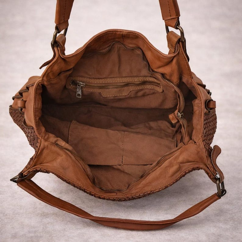 May include: Open view of a brown leather handbag with a woven side panel. The bag has two handles and a long shoulder strap. The interior features a zippered pocket and a large open space.