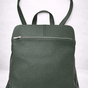K&ouml;nnte beinhalten: Ein dunkelgr&uuml;ner Lederrucksack mit einer Rei&szlig;verschlusstasche vorne und einem oberen Griff. Der Rucksack hat verstellbare Schultergurte und einen silbernen Rei&szlig;verschluss. Die Tasche ist aus strukturiertem Leder.