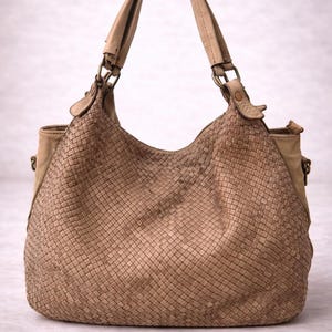 May include: A tan woven leather handbag with two handles and a shoulder strap. The bag has a large, rounded shape with a woven pattern on the front and sides. The handles and strap are made of a smooth, lighter-colored leather.