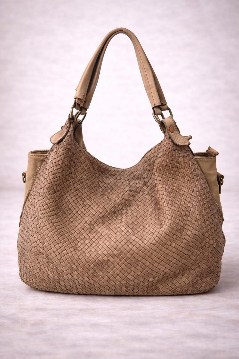 May include: A tan woven leather handbag with two handles and a shoulder strap. The bag has a large, rounded shape with a woven pattern on the front and sides. The handles and strap are made of a smooth, lighter-colored leather.