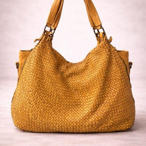 May include: Mustard yellow woven leather handbag with matching handles and a shoulder strap. The bag has a large, open design with a woven texture. The bag is a stylish accessory.